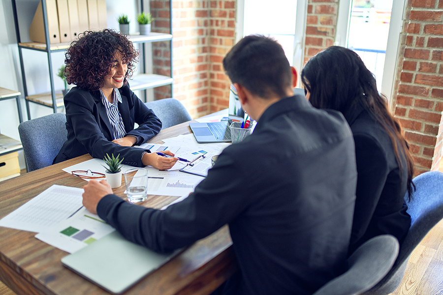 A couple sits at a desk with an agent discussing personal loan vs. personal line of credit.