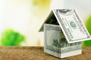 a house made out of one-hundred-dollar bills sits on a table, suggesting that current home prices are rising