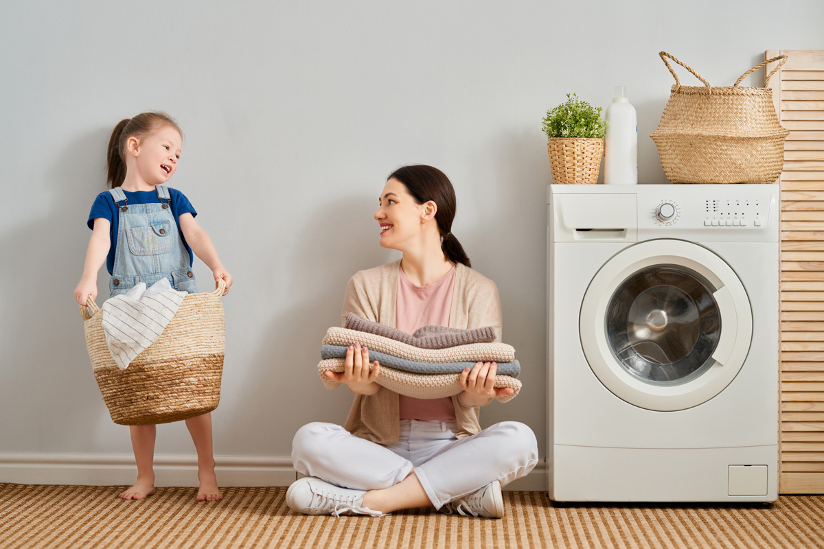 Beautiful young woman and child girl little helper are having fun and smiling while doing laundry at home.